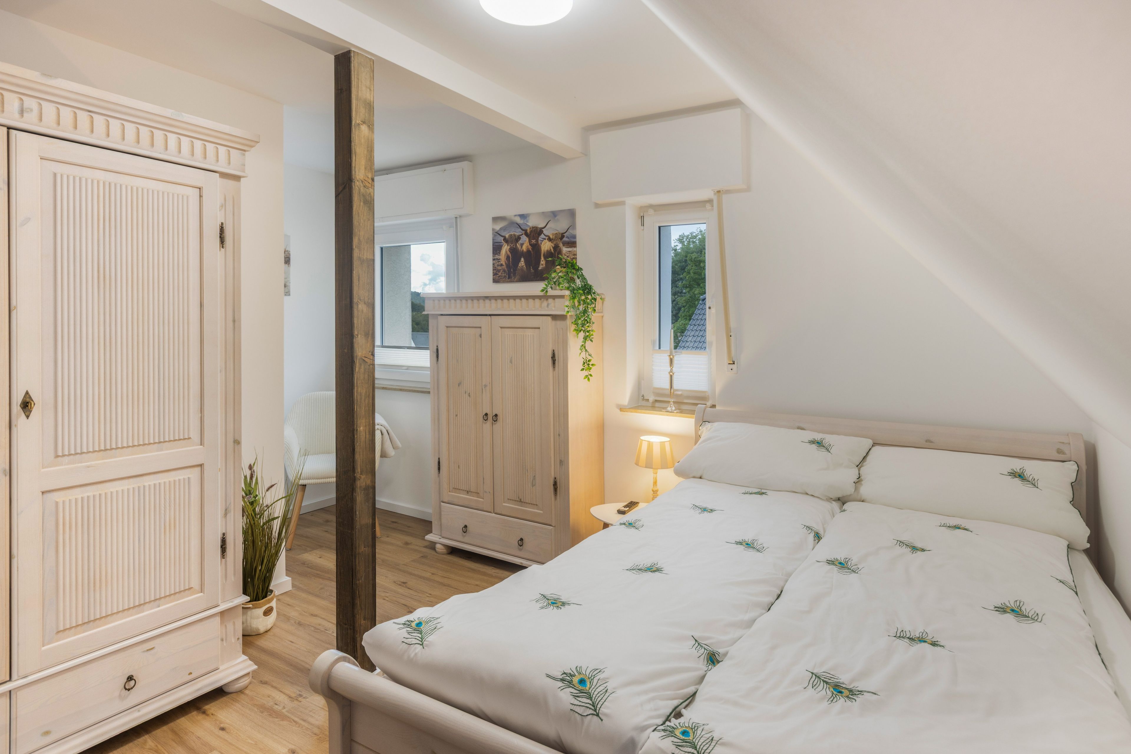 Une chambre à coucher avec un lit, une armoire, un miroir, une fenêtre et une plante.