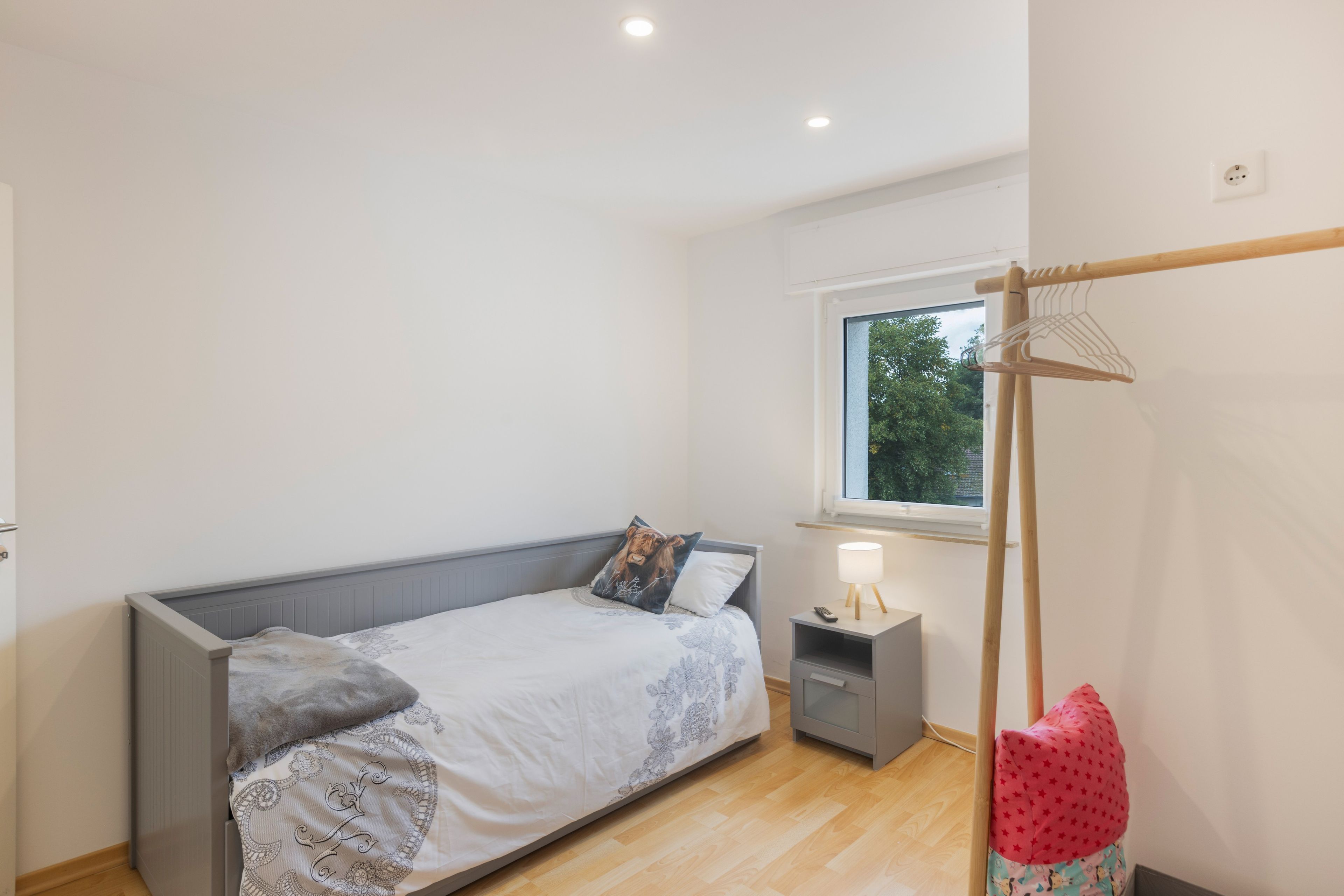 Ein Schlafzimmer mit Bett, Nachttisch, Lampe und Fenster.