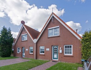 A two-story brick building with a pitched roof, a chimney, and a small garden area with a paved walkway. - Holiday Home With 2 Bedrooms (Krummhoern)