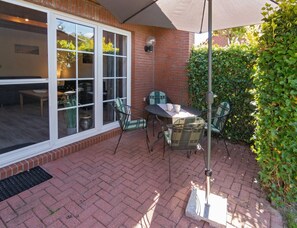 An outdoor patio with a brick floor, a table with chairs, and a large window. - Holiday Home With 2 Bedrooms (Krummhoern)