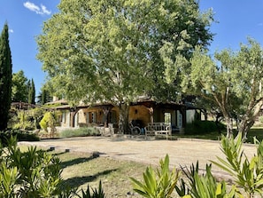 A rustic villa with a patio, surrounded by mature trees and a well-maintained garden. - Villa in Var With Swimming Pool (Cotignac)