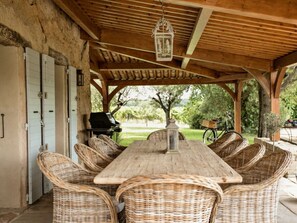 An outdoor covered patio with a wooden table and wicker chairs, a grill, and a bicycle. - Villa in Var With Swimming Pool (Cotignac)