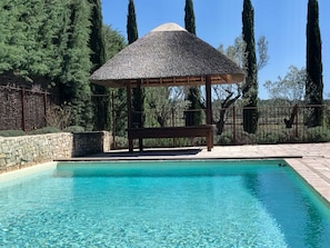 A swimming pool with a wooden bench and a thatched-roof gazebo. - Villa in Var With Swimming Pool (Cotignac)
