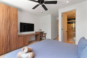 Ein modernes Schlafzimmer mit Bett, Schreibtisch, Fernseher und Deckenventilator.