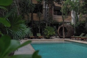 A pool area with lounge chairs and a building with a wooden facade. - Suk-Ha Condo with Rooftop | La Veleta, Tulum (Tulum)