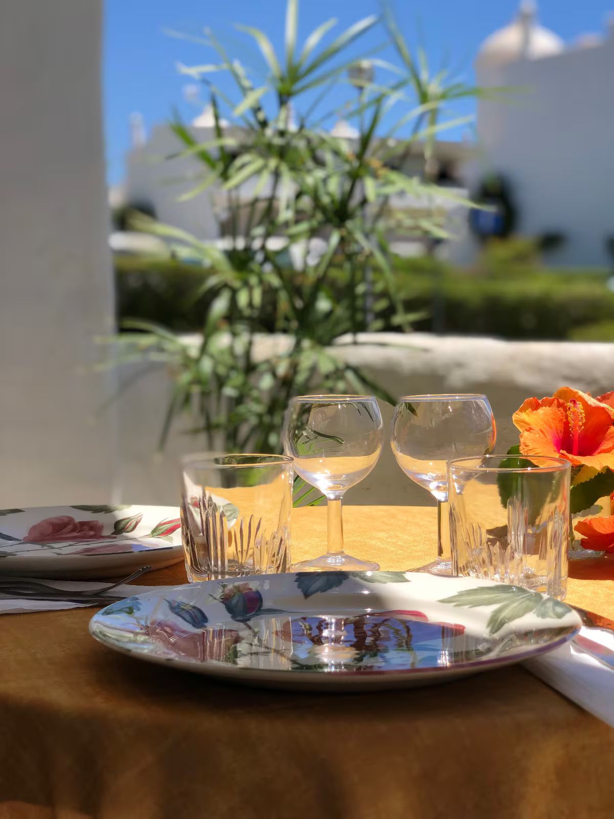 A table with a floral tablecloth, two wine glasses, and a plate with a floral design.