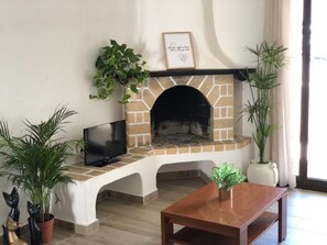 A living room with a brick fireplace, a flat-screen TV, and various potted plants. - A peaceful house with a swimming pool (Porches)
