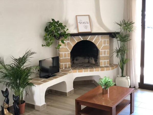 Un salon avec une cheminée en briques, un téléviseur à écran plat et diverses plantes en pot.