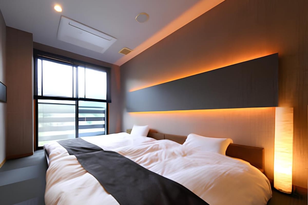 Habitación de hotel moderna con una cama grande, ventanal con vistas y un aplique de pared.