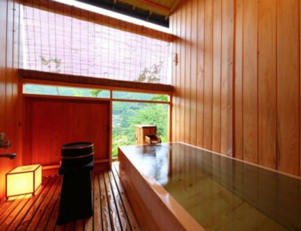 Ein Zimmer aus Holz mit einer Whirlwanne, einem Fenster und einem kleinen Holzschemel.