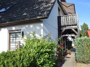 A house with a tiled roof, a balcony, and a garden with green shrubs and red flowers. - in the House of Four Oaks (Ostseebad Prerow)