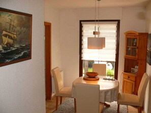 A dining area with a table, chairs, a painting, and a window with blinds. - in the House of Four Oaks (Ostseebad Prerow)