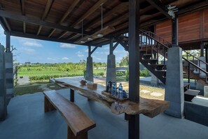 An outdoor dining area with a wooden bench and a table, a staircase, and a view of a green landscape. - Klumpu Uma Villa (Denpasar)