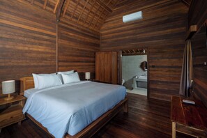 Une pièce aux murs lambrissés, comprenant un lit, des lampes de chevet, une armoire et une salle de bain visible à travers une porte ouverte.