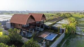 A two-story house with a curved roof, a swimming pool, and a garden with a pond. - Klumpu Uma Villa (Denpasar)