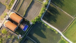 Vue aérienne d’un quartier résidentiel, avec une maison dotée d’une piscine, entourée de champs agricoles.