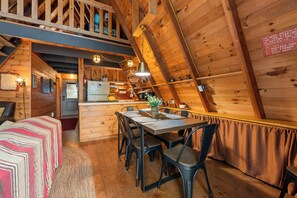 Un acogedor interior de cabaña con comedor, cocina y un altillo.