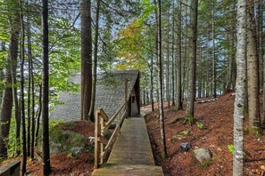 A wooden walkway leading to a cabin in a forested area. - Treetop Cabin | Waterfront on Mooselookmeguntic | Pet Friendly (Oquossoc)