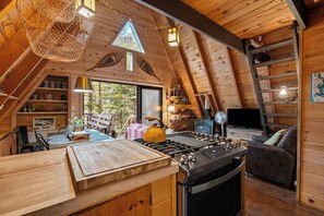 A cozy kitchen with a stove, a dining table, and a view of the outdoors. - Treetop Cabin | Waterfront on Mooselookmeguntic | Pet Friendly (Oquossoc)