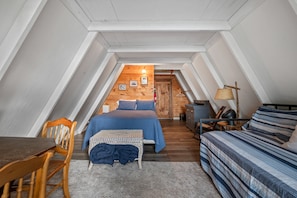 A cozy attic bedroom with a sloped ceiling, a bed, a desk, and a chair. - Treetop Cabin | Waterfront on Mooselookmeguntic | Pet Friendly (Oquossoc)