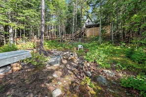 A rustic cabin with a wooden deck and stairs leading to a covered area. - Treetop Cabin | Waterfront on Mooselookmeguntic | Pet Friendly (Oquossoc)