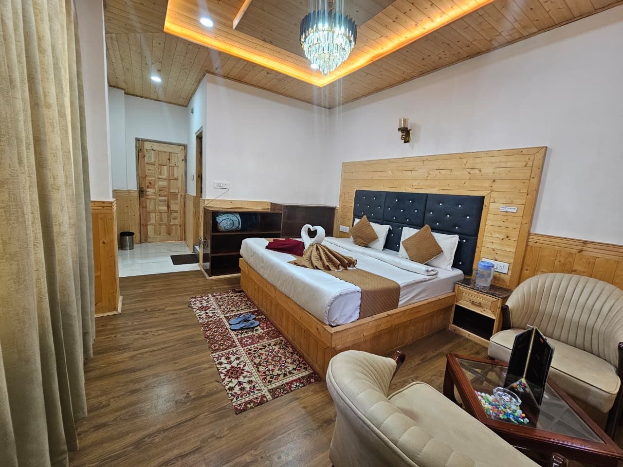 A bedroom with a wooden headboard, a bed with white bedding, a bedside table, a chair, and a small table with a lamp.