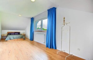 Ein Schlafzimmer mit Bett, einem fenster mit Vorhängen, einem Heizkörper und einer weißen Wand.
