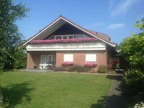 A two-story house with a sloped roof, a balcony with pink flowers, and a well-maintained lawn. - Prinsepark 1st Floor (Domburg)