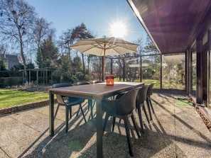 An outdoor patio with a table and chairs, a sun umbrella, and a view of the surrounding garden and trees. - Holiday Home With 4 Bedrooms (Burgh-Haamstede)