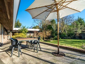 An outdoor patio with a table and chairs, a large umbrella, and a grassy area with trees. - Holiday Home With 4 Bedrooms (Burgh-Haamstede)