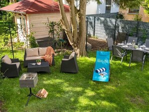 Ein Außenbereich mit Terrasse, einer Sofagarnitur, einem Grill und einem Esstisch mit Stühlen.