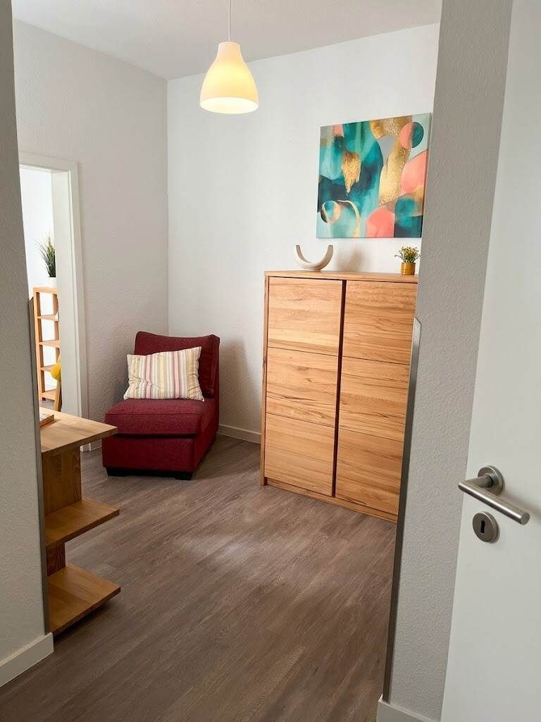 A compact room with a red sofa, a wooden cabinet, and a hanging pendant light.