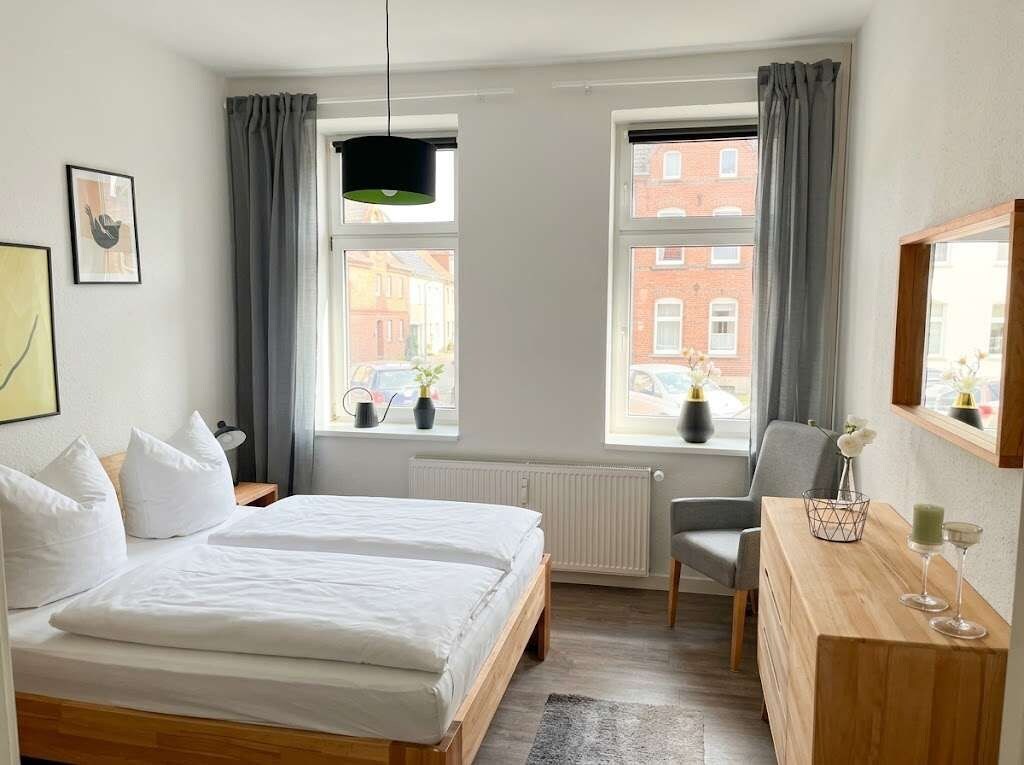 Ein Hotelzimmer mit einem Bett, einem Schreibtisch, zwei Fenstern und Blick auf Gebäude.