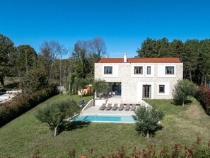 Ein zweistöckiges Steinhaus mit Swimmingpool, umgeben von einer gepflegten Rasenfläche und Bäumen.