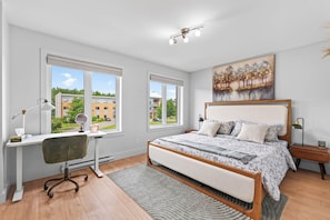 A bedroom with a bed, a desk, and a window with a view of buildings. - L'Écrin: Contemporary elegance and cozy comfort in the heart of the city. (Québec)
