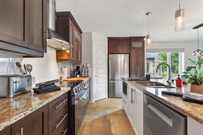 A modern kitchen with stainless steel appliances, granite countertops, and wooden cabinets. - L'Écrin: Contemporary elegance and cozy comfort in the heart of the city. (Québec)