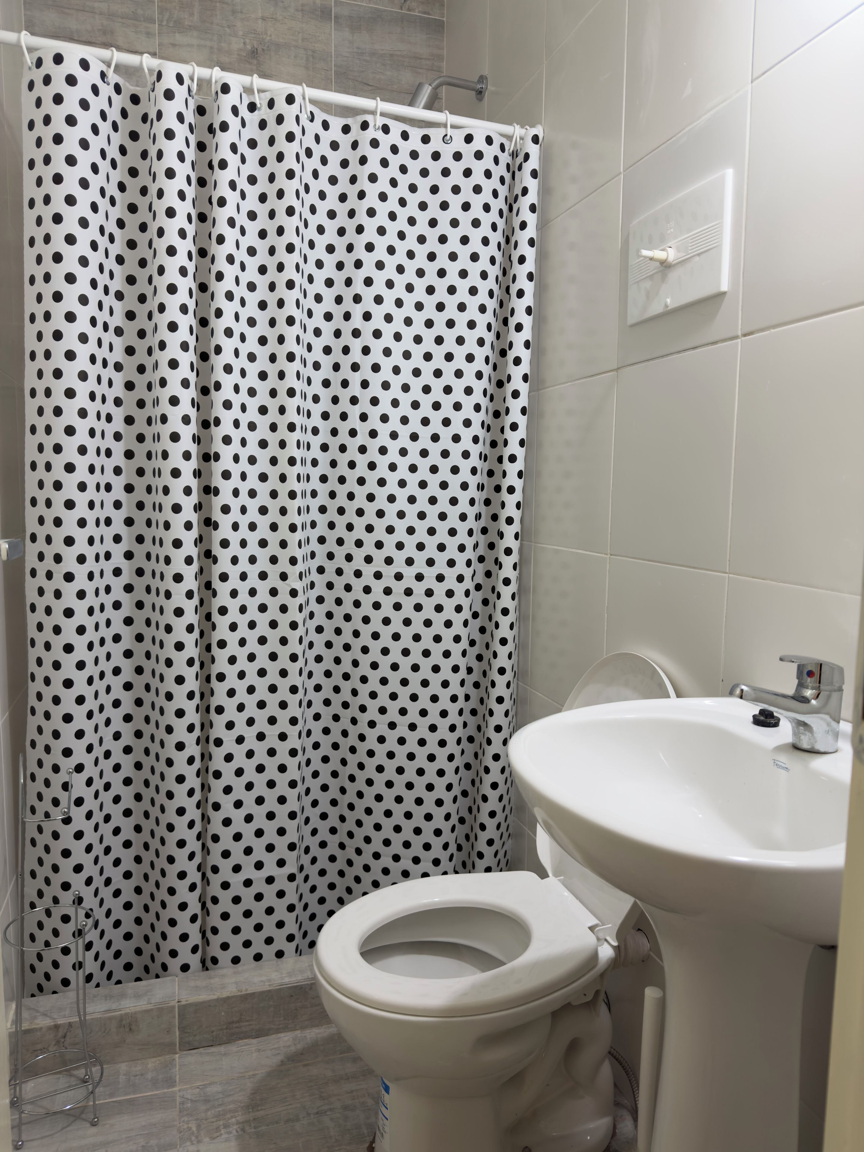 Un baño con un inodoro blanco, un lavamanos blanco y una cortina de ducha con estampado de lunares negros.