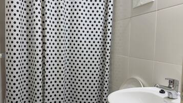 Un baño con un inodoro blanco, un lavamanos blanco y una cortina de ducha con estampado de lunares negros.