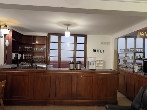 A bar area with a wooden counter, a water dispenser, and shelves with glasses and cups.