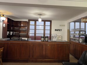 A bar area with a wooden counter, a water dispenser, and shelves with glasses and cups.