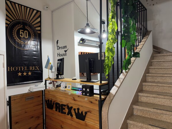A hotel reception desk with a 'Dream House' sign, a '50 years' anniversary banner, and a staircase with greenery.