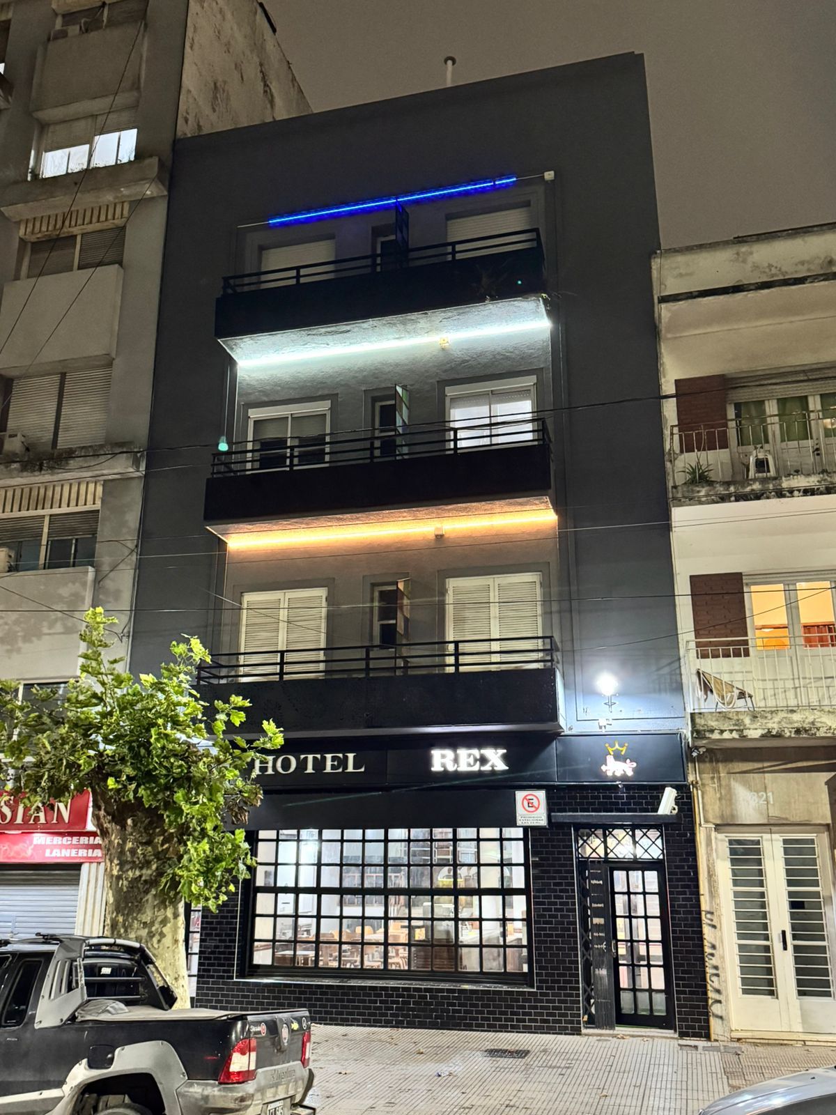 Un hotel de varios pisos con un llamativo letrero que dice 'HOTEL REX', grandes ventanales y un balcón en el piso superior.
