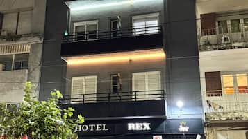 Un hotel de varios pisos con un llamativo letrero que dice 'HOTEL REX', grandes ventanales y un balcón en el piso superior.