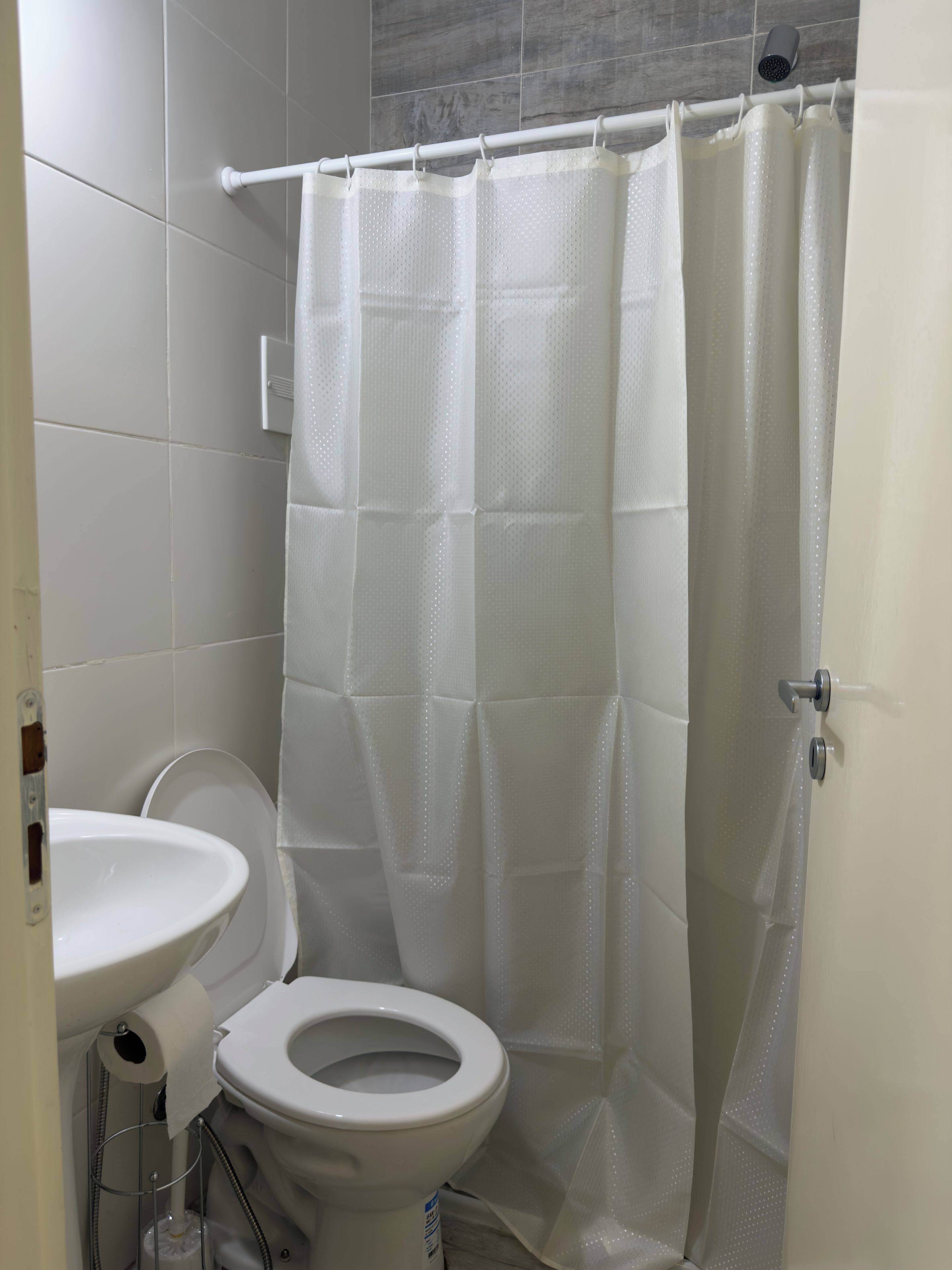 Un baño con inodoro blanco, lavamanos y cortina de ducha.
