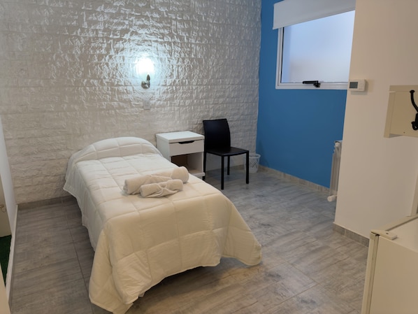 A room with a bed, a chair, a small table, and a window.