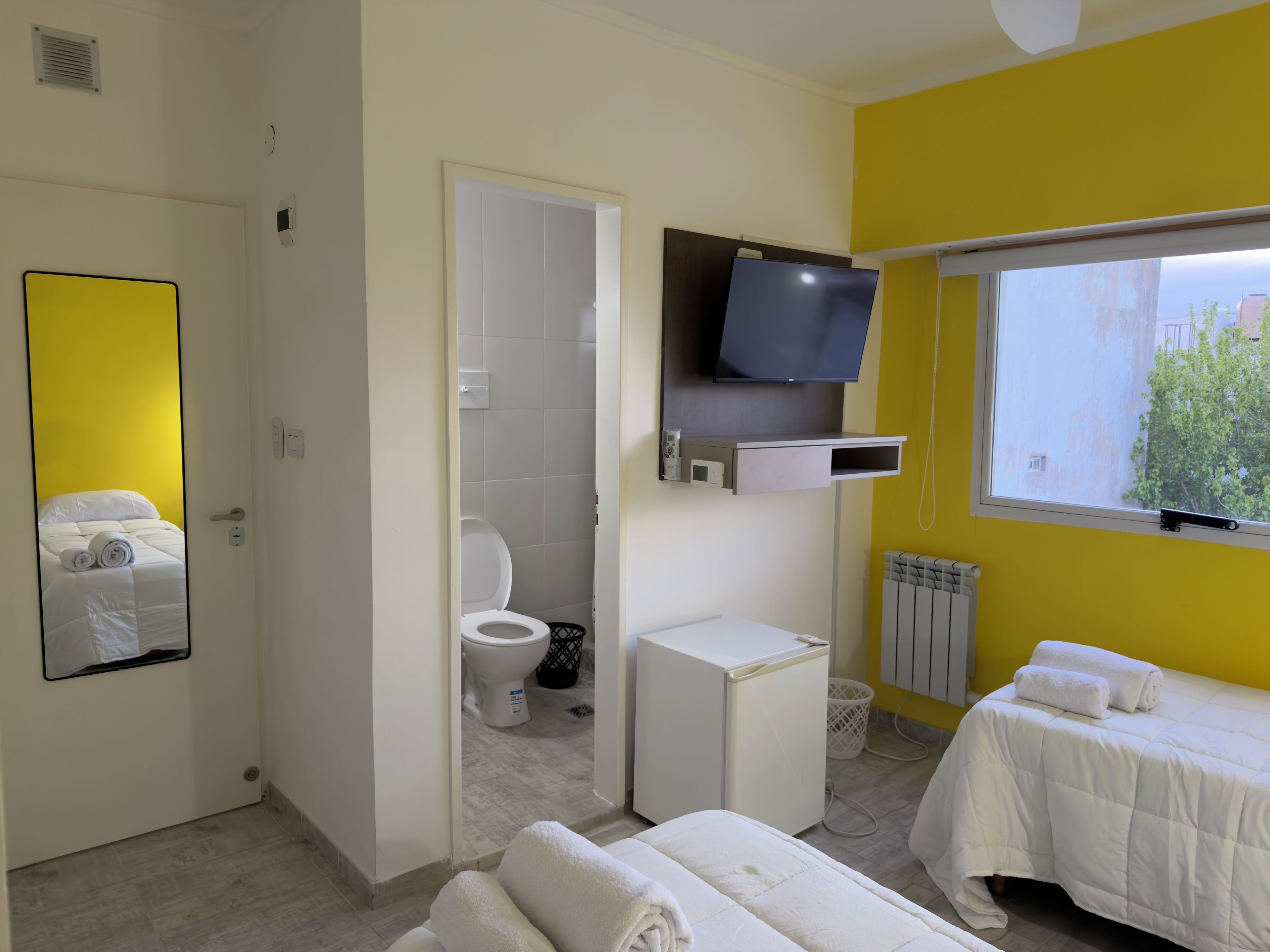 Habitación de hotel con cama, televisión, inodoro y ventana.