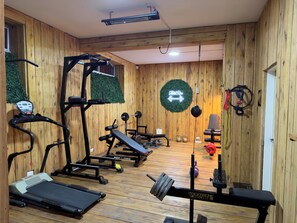 A gym with wooden walls, a treadmill, weight machines, and a wall-mounted neon sign.