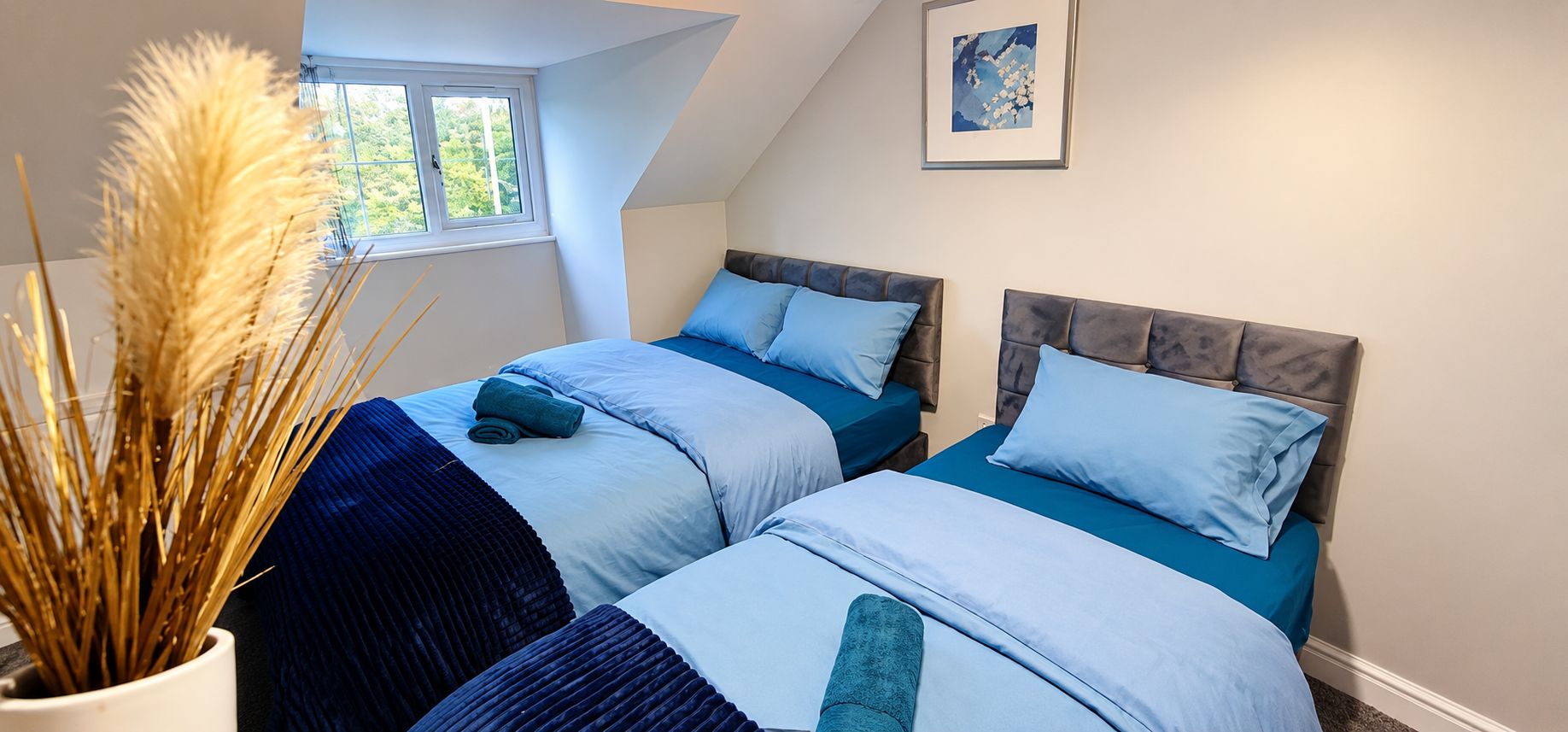 A bedroom with two beds, a window, and a framed picture on the wall.