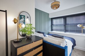 A bedroom with a bed, bedside table, lamp, and a window with blinds. - Host Stay - The Enterprise Suite (Middlesbrough)
