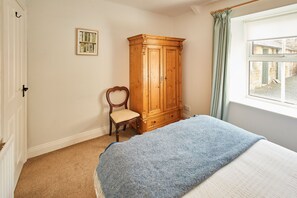 A bedroom with a bed, a wooden wardrobe, a chair, a framed picture on the wall, and a window with curtains. - Host and Stay - The Cottage ALN (Alnwick)